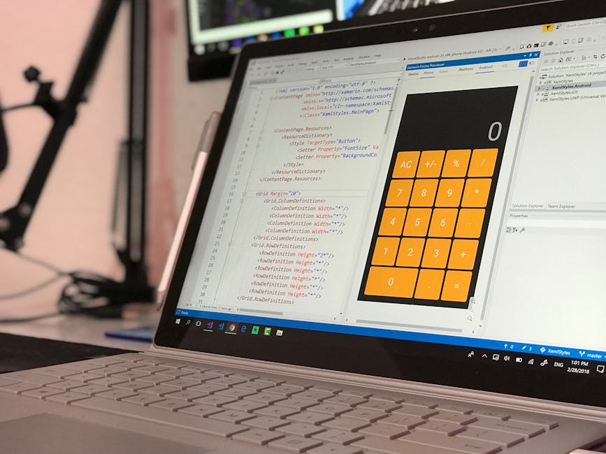 A close-up view of a silver laptop placed on a desk, displaying a code editing software on the left side of the screen with lines of HTML/CSS code visible, and a large orange calculator application on